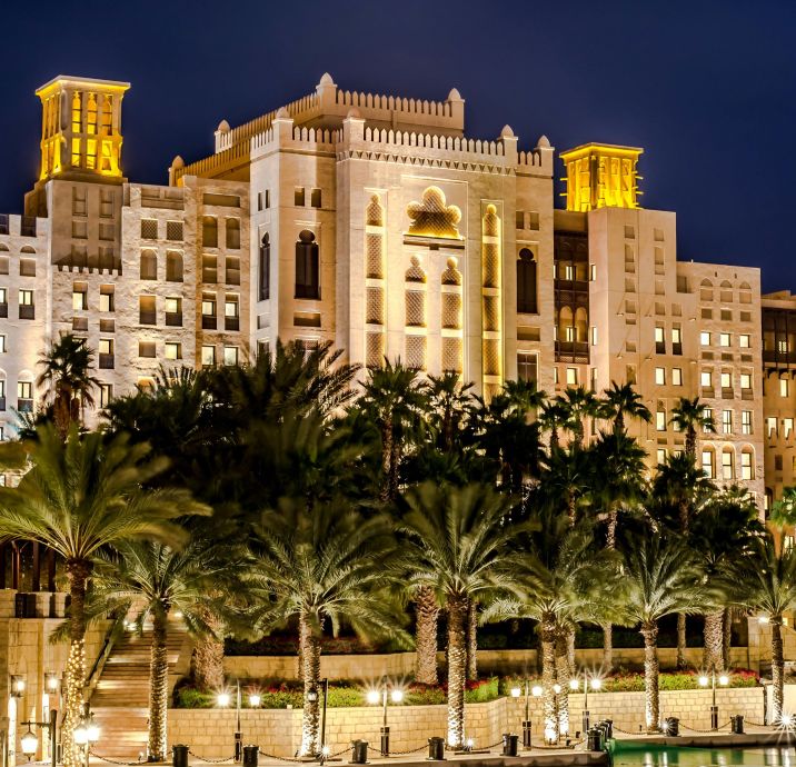 A stunning night view of a luxurious hotel with palm trees reflecting on water in Dubai.