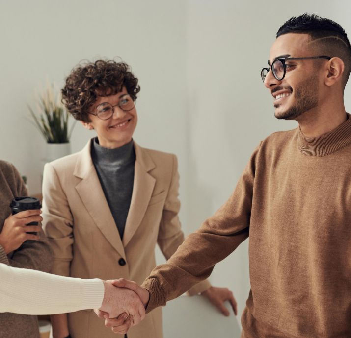 Diverse group of young adults shaking hands in an office environment, depicting teamwork and collaboration.